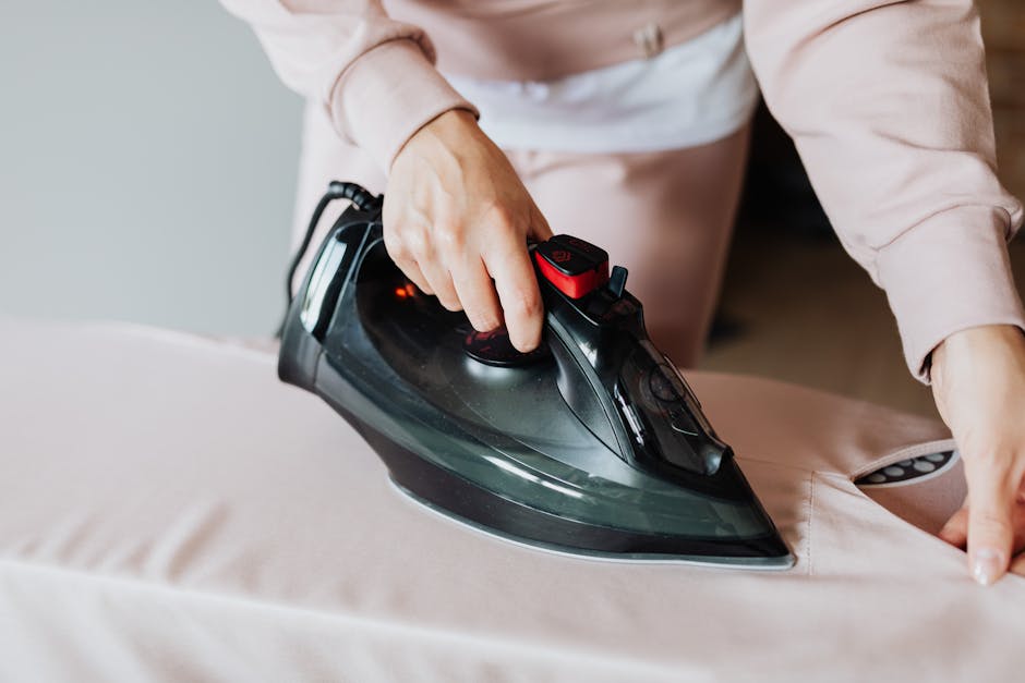 A light blue dustpan and a wooden-handled brush with natural bristles hanging on a plain, smooth, light grey wall, illuminated by soft, natural lighting to highlight their clean and well-maintained su